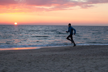 young man in atumn clothes training on the beach, sunrise background, male runner at morning  