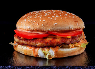 Burger with beef chops, tomatoes, salad, cheese and ketchup, in a fresh bun with sesame, on a black stone tray.