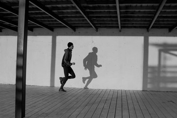 black and white picture of male runner training, shadow of runner on white wall 