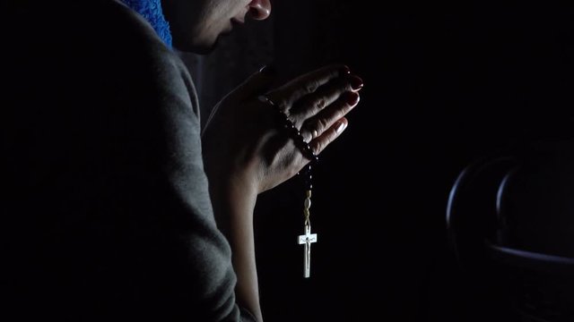 A woman praying with a rosary in the dark