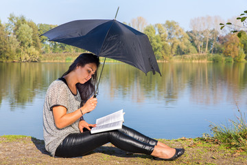 Woman with umbrella reading book in nature