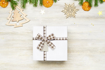 Christmas background. Square gift box with bow. The branches of fir, dried orange, star foil, fir cone, wooden toys in the shape of Christmas trees and snowflakes