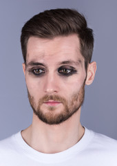 Obraz premium Vertical portrait of a young man with dirty makeup. Sad, looking down. Beard and mustache