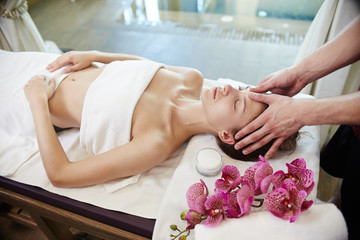 High angle portrait of young woman enjoying face and head massage lying on table in SPA center and...