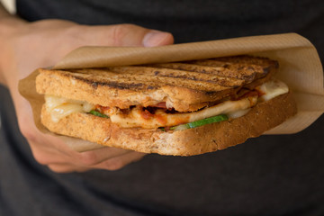 grilled panini with chicken and tomatos on wooden board  close up in mans hand