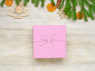 Christmas background. Pink gift box with a bow of twine. Spruce branches, toys, cones, orange slices on a white wooden background.