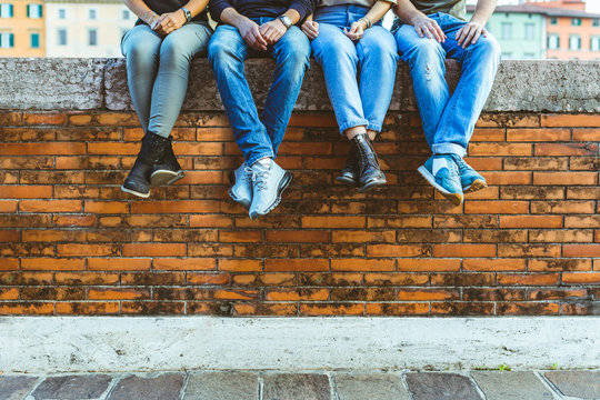 Legs of four teenagers sitting on a bricks wall