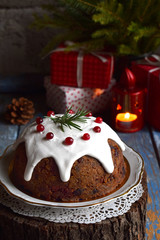 Traditional english Christmas steamed pudding with winter berries, dried fruits, nut in festive setting with Xmas tree and burning candle. Fruit cake