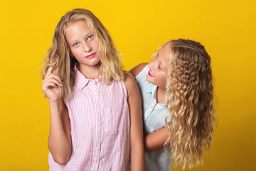 Funny girls twins have fun together on yellow background.