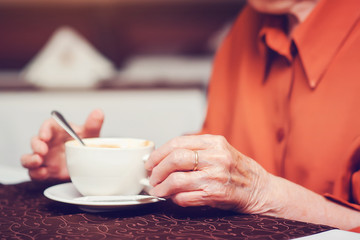 elderly female hands with cup of coffee, aged woman in cafe