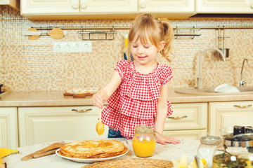 Cute little girl prepare pancakes and pouring honey on stack of pancakes.