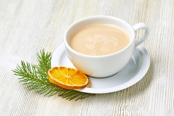 Coffee Cup cappuccino and saucer on a light wooden background decorated with fir branch and dried orange slice. Christmas morning.