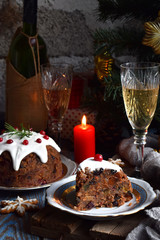 Fototapeta na wymiar Traditional english Christmas steamed pudding with winter berries, dried fruits, nut in festive setting with Xmas tree, burning candle and glass of white wine, champagne. Fruit cake