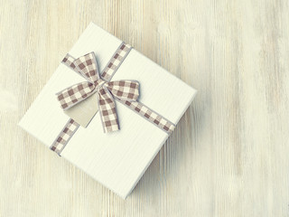 Gift box with ribbon in a cage on a light wooden background. The view from the top.