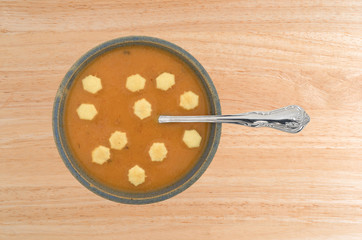 A serving of salmon bisque soup in an old stoneware bowl with a spoon in the food plus several crackers on a wood table top.