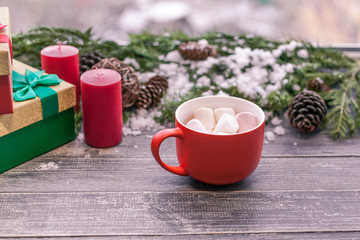 Big cup cocoa from marshmallows on a wooden table on a background of Christmas composition. New Year's still life. Fir-tree branches, cones, gift boxes