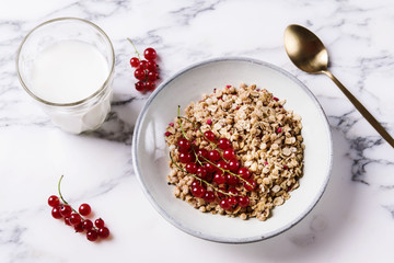 Healthy breakfast of muesli and glass of milk with red currant decor on grey marble table. Selective focus 