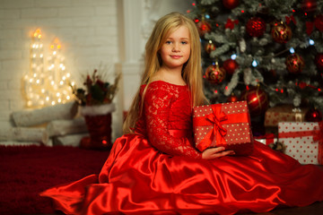 Portrait of pretty blonde girl is wearing fashion red dress near decorated xmas tree