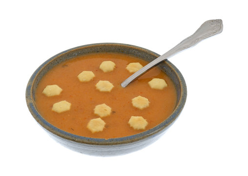 A serving of salmon bisque soup in an old stoneware bowl with a spoon in the food plus several crackers isolated on a white background.
