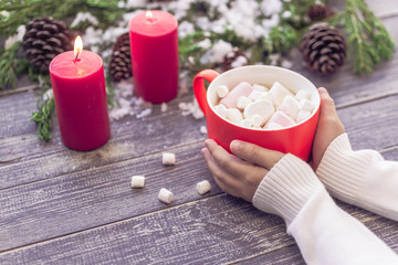 Children's hands hold a cocoa cup from marshmallows on a wooden table on a background of Christmas composition. New Year's still life. Fir-tree branches, cones, gift boxes