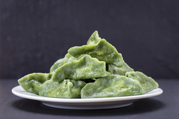 Green dim sum, chinese food. Delicious homemade dumplings with beef meat or mashed potatoes or cottage cheese in the dough, together with spirulina on a black slate background