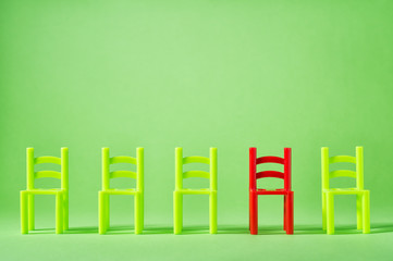 Unique red chair in row of green others. Leadership concept. Empty chairs by wall. The concept of uniqueness, distinction from others.