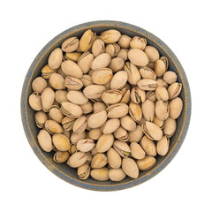 Top view of a stoneware bowl filled with roasted pistachio nuts isolated on a white background.