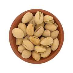 Top view of a small red clay bowl filled with roasted pistachio nuts isolated on a white background.