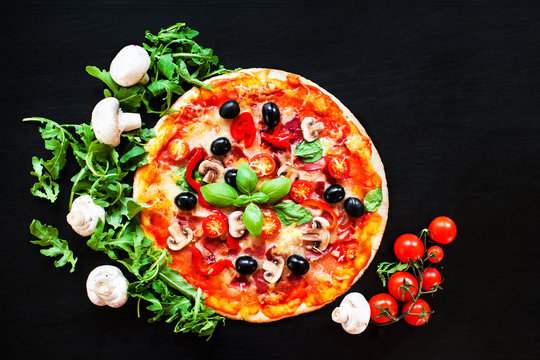 Hot pizza with Pepperoni Sausage on a dark background  with copy space. Pizza with mushrooms, tomatoes, cheese, onion, oil, pepper, salt, basil, olive