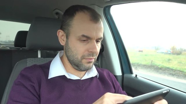 Businessman using a tablet while sitting inside car. Man with a tablet-pc in the  vehicle.