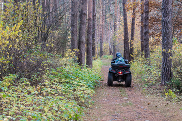 ATV quad with driver and passenger on magic picturesque path in the autumn forest