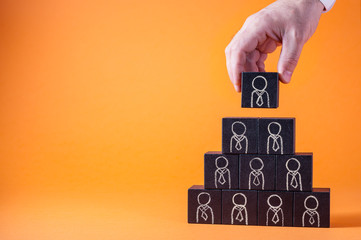 Man's hand holding a top of wooden blocks pyramid over wooden table. Business concept for human...