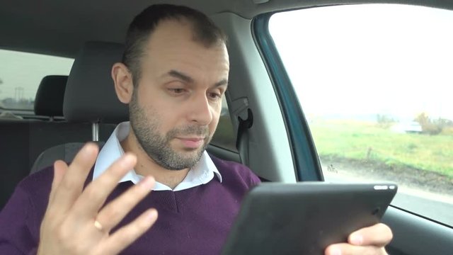 Successful young businessman is video chatting, as seen from tablet-pc. Man talking  on video call on tablet, sitting in the car.
