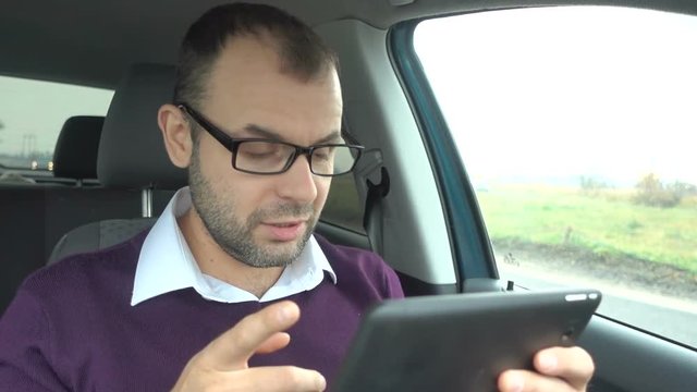 Successful young businessman is video chatting, as seen from tablet-pc. Man talking  on video call on tablet, sitting in the car.