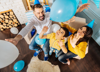 Excellent party. Cheerful little boy and his parents sitting on the sofa together and having fun...