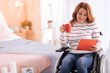 Coffee break. Attractive smiling blond disabled woman of middle age holding her cup and a notebook...