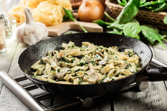 Tagliatelle pasta with spinach and mushrooms on a pan.