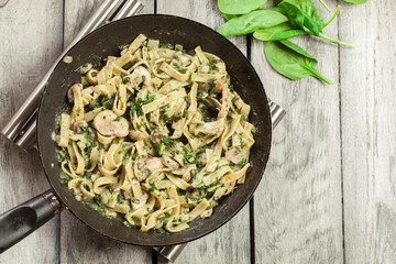 Tagliatelle pasta with spinach and mushrooms on a pan.