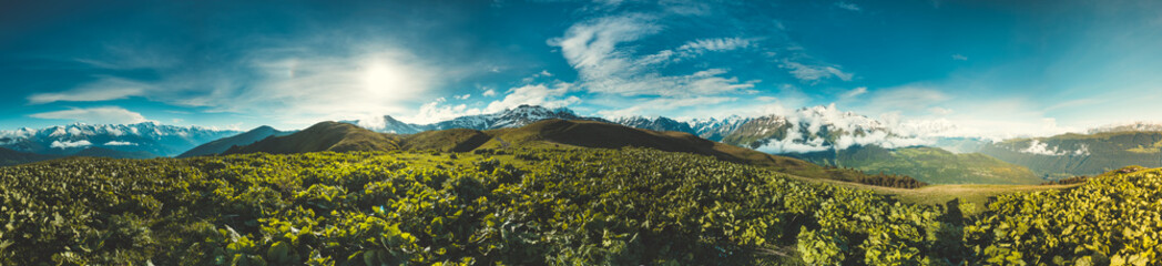 Panorama of summer landscape with green hills and mountain snow capped peaks against blue cloudy sky. Svanetia region, Georgia. Main Caucasian ridge. Holiday, hiking, sport, recreation