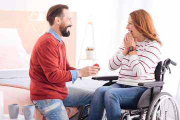 Making a proposal. Happy smiling bearded man making a proposal to a pretty blond handicapped woman smiling and her face expressing surprise and excitement and she sitting in a wheelchair