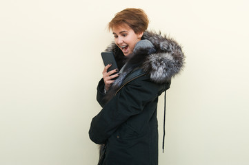 Happy girl in a fur coat uses a phone. she is very happy.