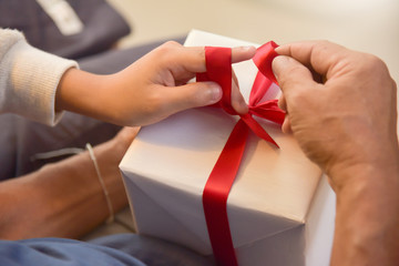 Asian boy and elderly man holding on red ribbon of white gift box.