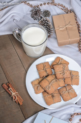 A cup of milk, cinnamon sticks and homemade cookies in a Christmas decor.
