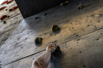 Hand of the young man on a hook of the artificial climbing wall