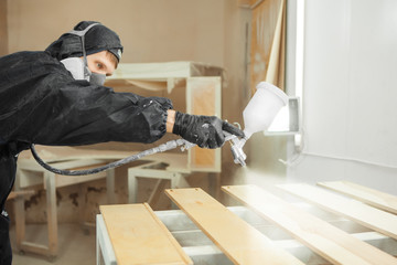 Man in respirator mask painting wooden planks at workshop.