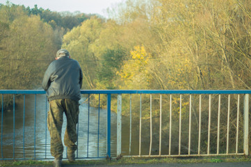 an old man stands on the bridge and looks at the river in autumn