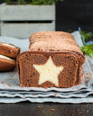 A very chocolate cake covered with dark chocolate and sprinkled with cocoa with a vanilla star inside. On a wooden dark background. Decorated with fresh cranberries, The perfect cool Christmas dessert