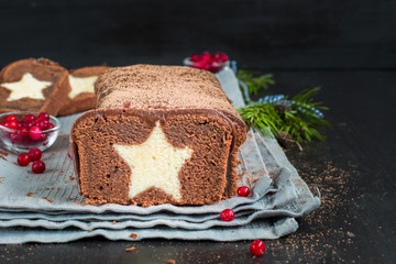 A very chocolate cake covered with dark chocolate and sprinkled with cocoa with a vanilla star inside. On a wooden dark background. Decorated with fresh cranberries, The perfect cool Christmas dessert