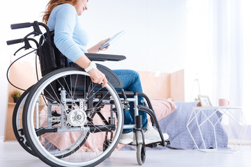 Avid reader. Blond smiling handicapped woman of middle age wearing a watch and a blue sweater and holding a book while sitting in a wheelchair
