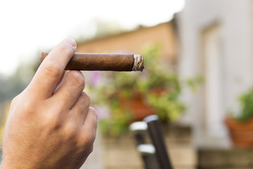 Detail of the hand of a smoking man holding a burning cigar with a blurred background